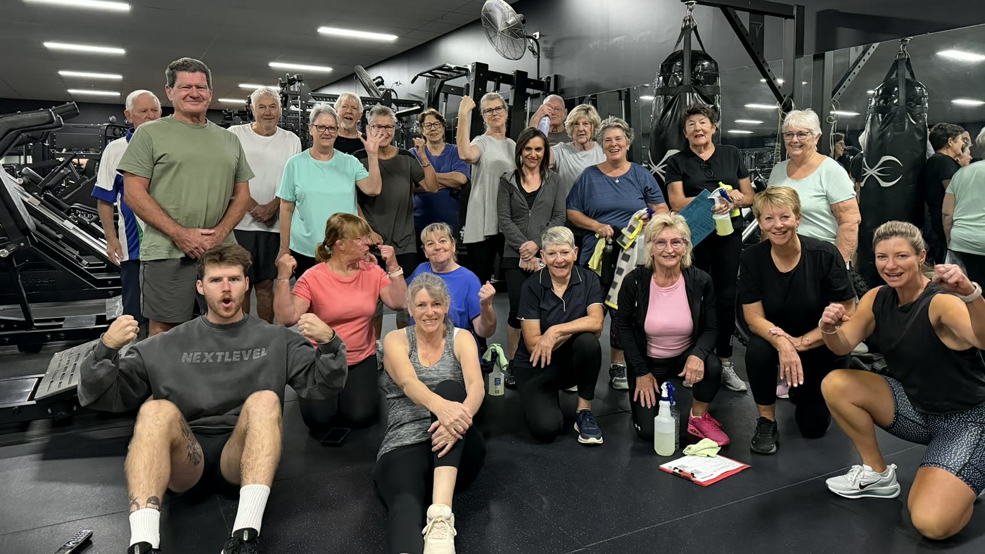Over 60s members of the Tuesday Active Adults class smiling and flexing on the gym floor with their instructors